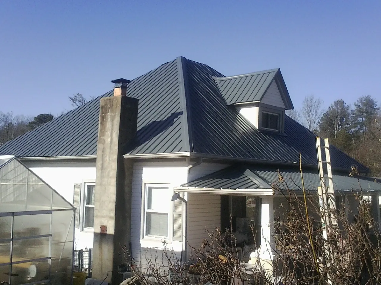Dark blue standing seam metal roof on a white farmhouse with dormer — Slate & Tile Roof Repair by Roofing Brothers in Holderness
