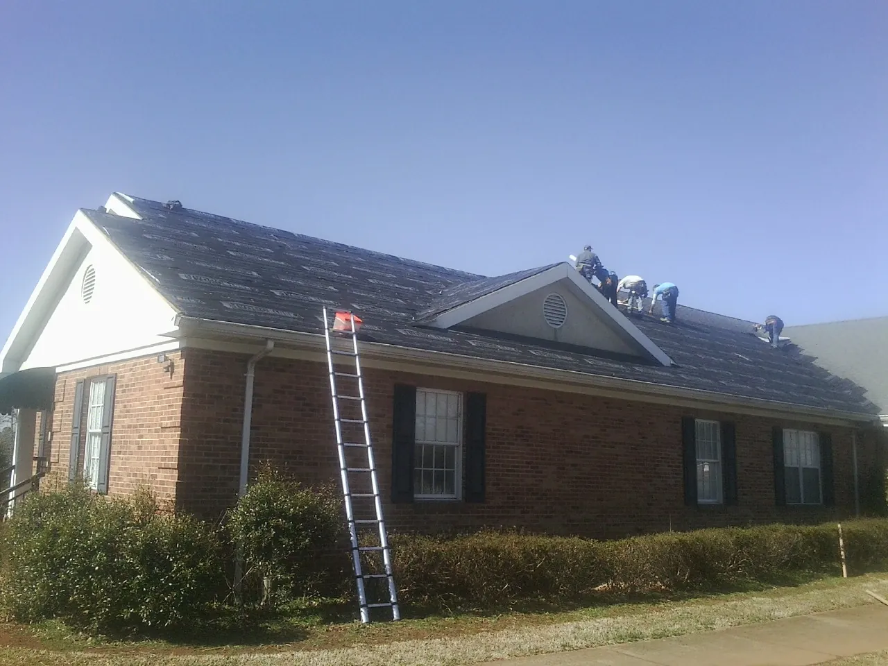 Crew tearing shingles off a brick ranch roof with a ladder set — Emergency Roof Repair work by our crew in Holderness
