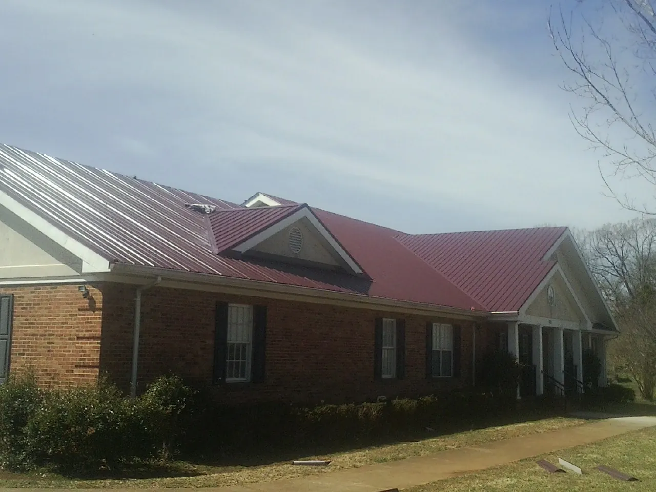 Red metal roof with gabled entries on a long brick building, from a Hail Damage Roof Repair job in Holderness