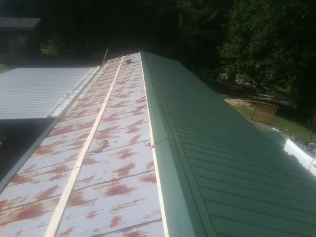 Old rusted panels beside newly installed green metal roofing — Wind Damage Roof Repair by Roofing Brothers in Holderness