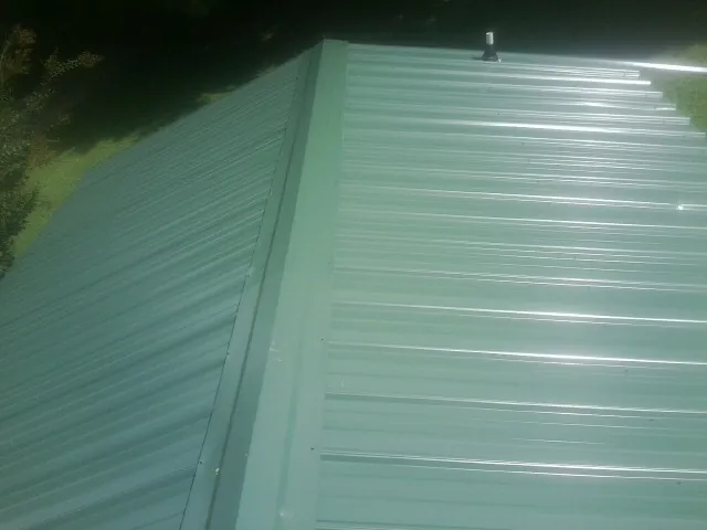New green metal panels meeting at the ridge of a roof — Flat Roof Repair work by our crew in Holderness