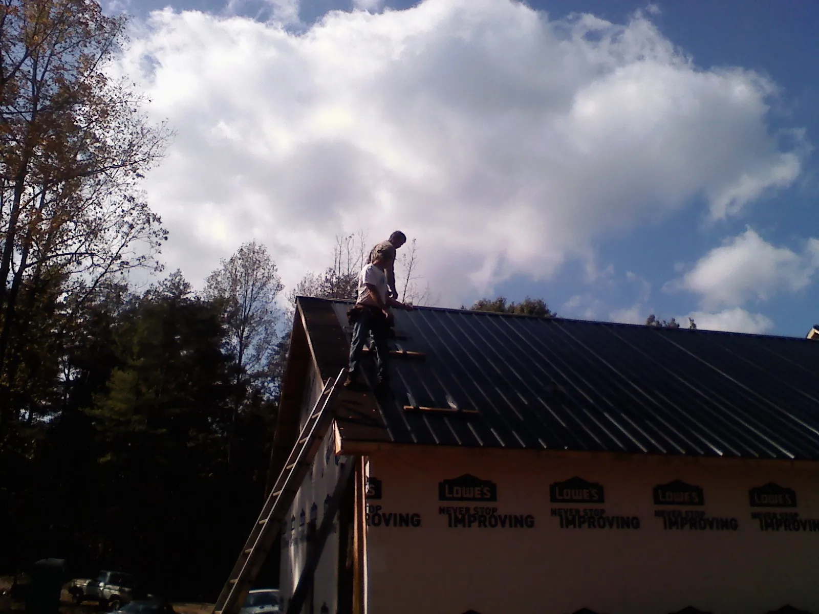 Roofer fastening dark metal panels high against a cloudy sky, from a Roof Inspection job in Holderness