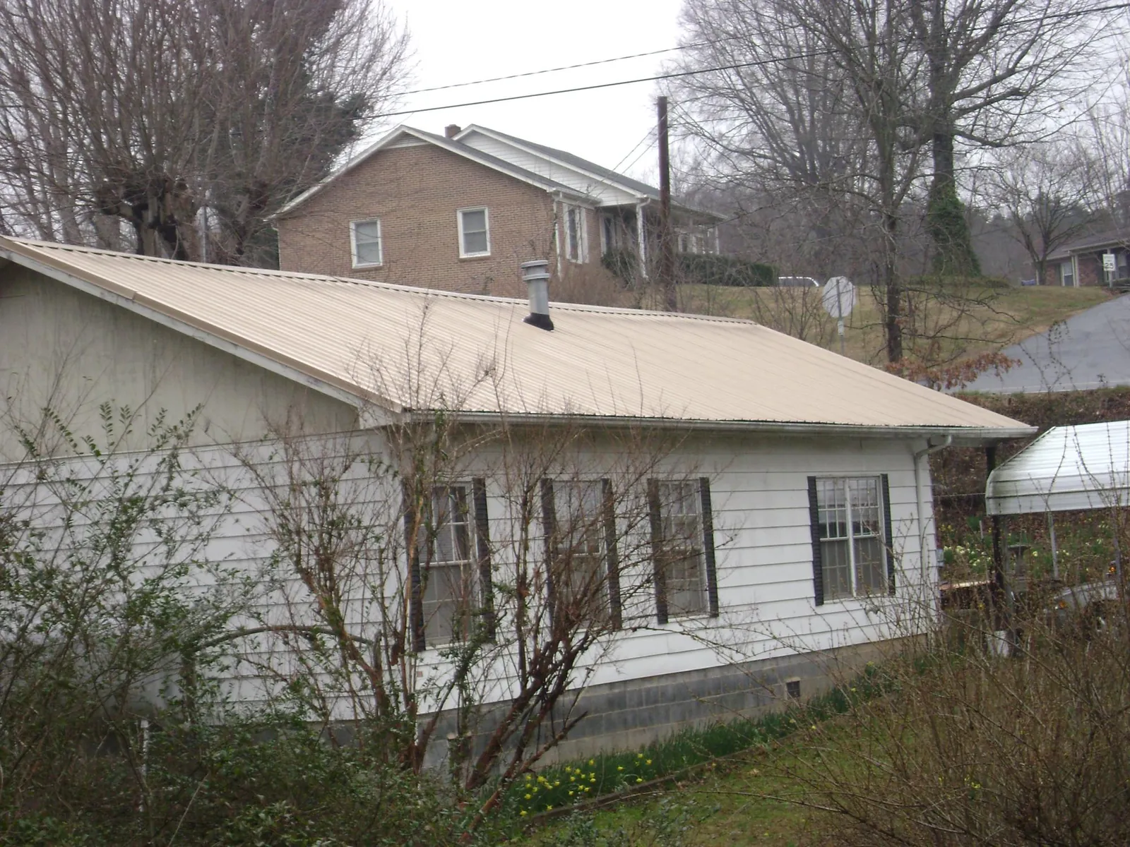 Tan metal roof on a white sided house set into a hillside — Commercial Roofing by Roofing Brothers in Holderness