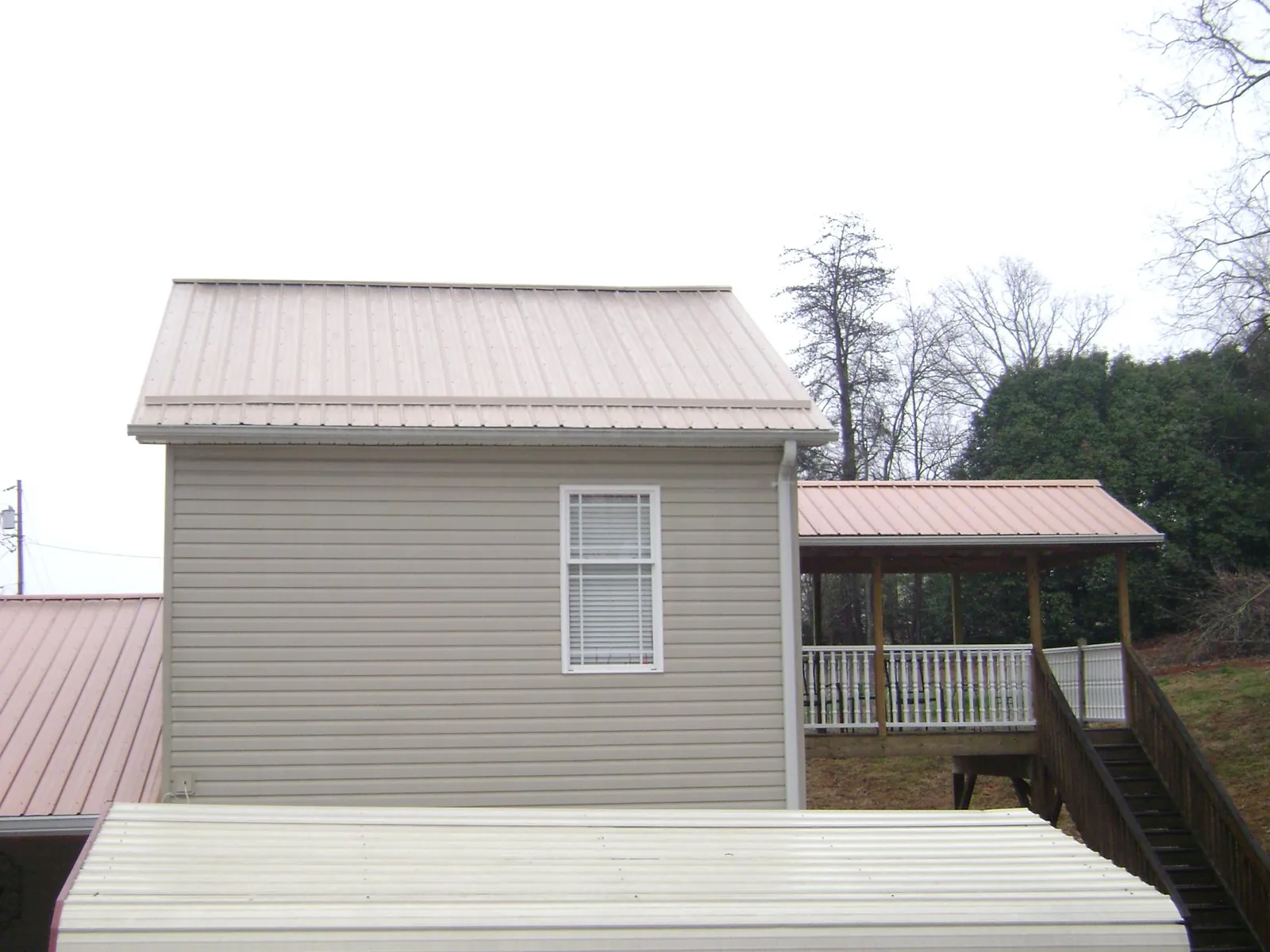 Tan metal roofs on a two story addition and attached porch, from a Roof Replacement job in Holderness